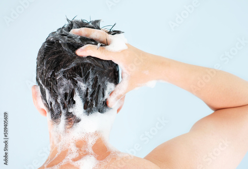 Male hands wash their hair with shampoo and foam on gray background, rear view.