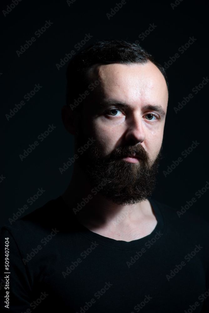 dramatic portrait of bearded millennial on black background