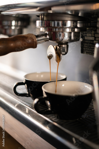 Two cups of coffee being poured from a espresso machine.