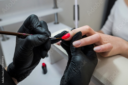  hands of a manicurist paints the nails of a client with red varnish.