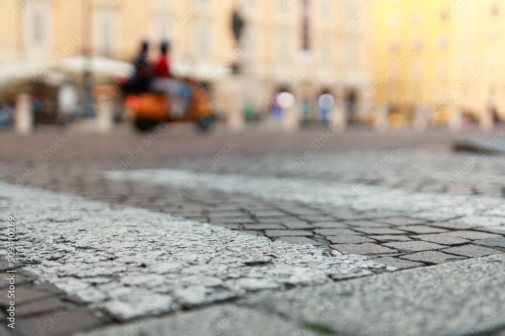 Stone pavement in perspective. Old street paved with stone blocks with white lines. Shallow depth of field. Vintage grunge texture. City ​​and people on background.