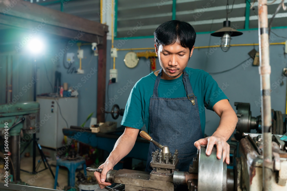 close-up, Asian technician Controlling small steel turning industrial tools, supervised by skilled technicians who stand behind the machine platform to supervise the steel turning process. close-up, Asian technician Controlling small steel turning industrial tools, supervised by skilled technicians who stand behind the machine platform to supervise the steel turning process.
