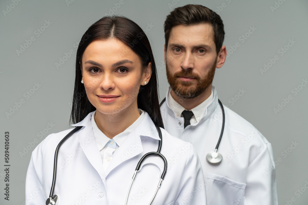 Male and female doctors in white medical jackets smiling at the camera while posing isolated on grey background Male and female doctors in white medical jackets smiling at the camera while posing isolated on grey background