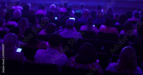 Audience, men and women, listening to a lecturer on a seminar and discussing information. Large room, subdued lighting. Back view. Education concept.