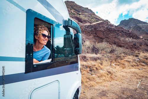 Happy adult woman smile and enjoy travel destination inside her camper van. Cheerful female people enjoy travel with camper van. Concept of van life and people renting motor home. Off grid parking