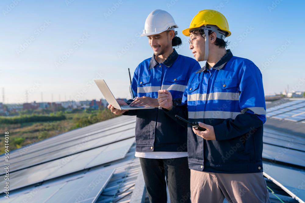Specialist technician professional engineer with laptop and tablet maintenance checking installing solar roof panel on the factory rooftop under sunlight. Engineers team survey check solar panel roof. Specialist technician professional engineer with laptop and tablet maintenance checking installing solar roof panel on the factory rooftop under sunlight. Engineers team survey check solar panel roof.