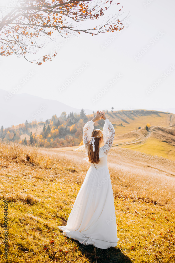 Stylish bride in a white dress posing in the autumn mountains among the yellow grass
