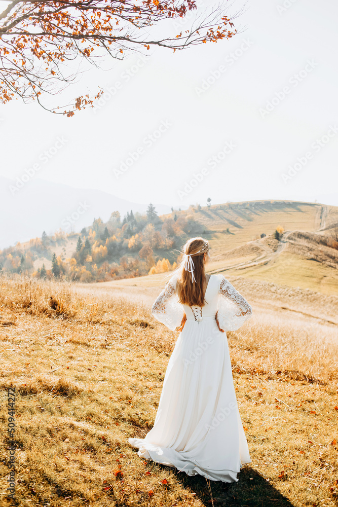 A beautiful bride in a white dress posing in the autumn mountains among the yellow grass