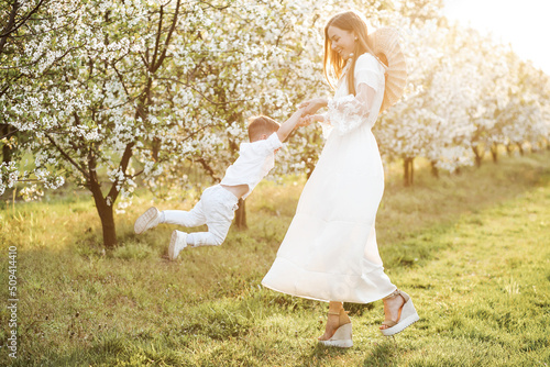 Mom holds her son's arms and spins around. Blooming garden in spring. © Yuliia