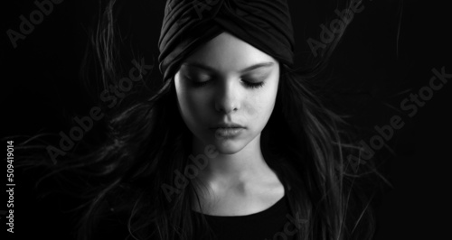 Black and white portrait of beautiful little teenager girl with turban and flowing hair is posing with meditative facial expression. Selective focus  low key