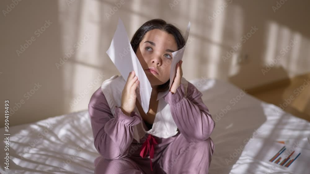 Overwhelmed exhausted little woman with graphs sitting on bed at home holding head in hands sighing. Portrait of tired Caucasian freelancer indoors in bedroom. Overworking and burnout Overwhelmed exhausted little woman with graphs sitting on bed at home holding head in hands sighing. Portrait of tired Caucasian freelancer indoors in bedroom. Overworking and burnout