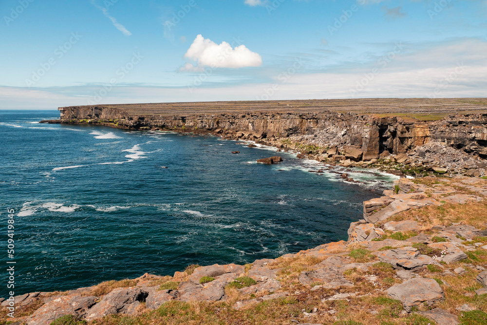 Wild rough stone coastline with cliffs of Aran island. county Galway, Ireland. Irish landscape. Warm sunny day. Blue cloudy sky. Travel and tourism area. Stunning nature scene.