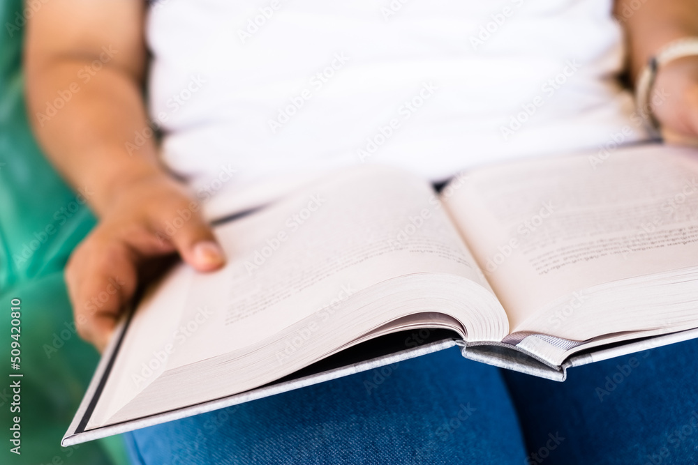 Closeup a woman is sitting on the chair and reading a book that rest on her lap, focus at the book Closeup a woman is sitting on the chair and reading a book that rest on her lap, focus at the book