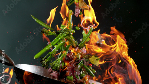 Closeup of chef throwing beef pieces with vegetable.