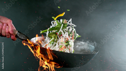 Closeup of chef throwing vegetable noodle mix from wok pan in fire. photo
