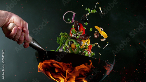 Vászonkép Closeup of chef throwing vegetable mix from wok pan in fire.