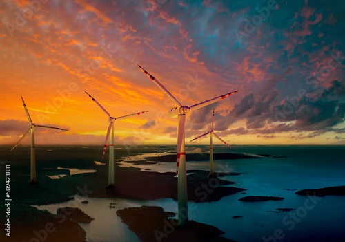 Windmills next to lake. Wind turbines at sunset. Stations for obtaining energy from wind. Wind turbines on banks of river. Regenerative energy concept. Windmills offshore. Natural source of energy