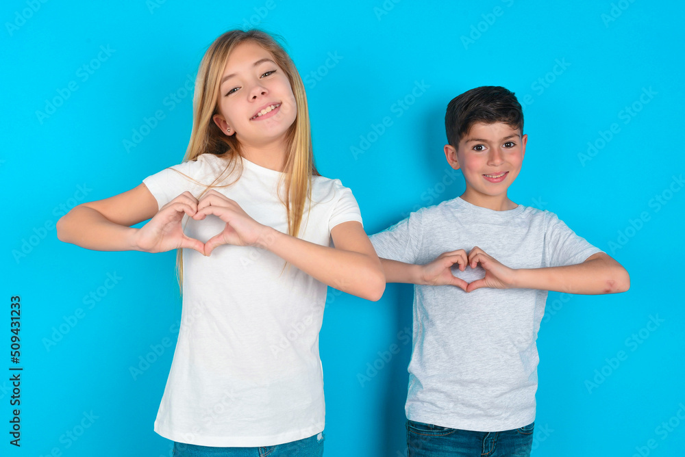two kids boy and girl standing over blue studio background smiling in love showing heart symbol and shape with hands. Romantic concept. two kids boy and girl standing over blue studio background smiling in love showing heart symbol and shape with hands. Romantic concept.