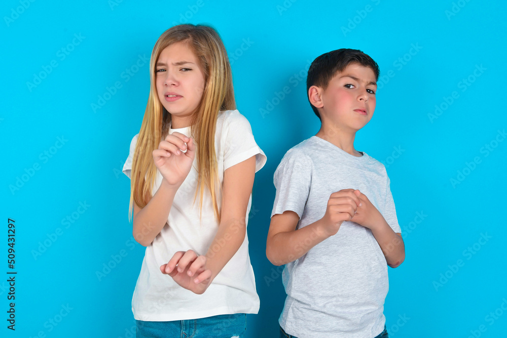 Ugh how disgusting! Displeased two kids boy and girl standing over blue studio background, has dissatisfied facial expression as sees something abominable. Ugh how disgusting! Displeased two kids boy and girl standing over blue studio background, has dissatisfied facial expression as sees something abominable.