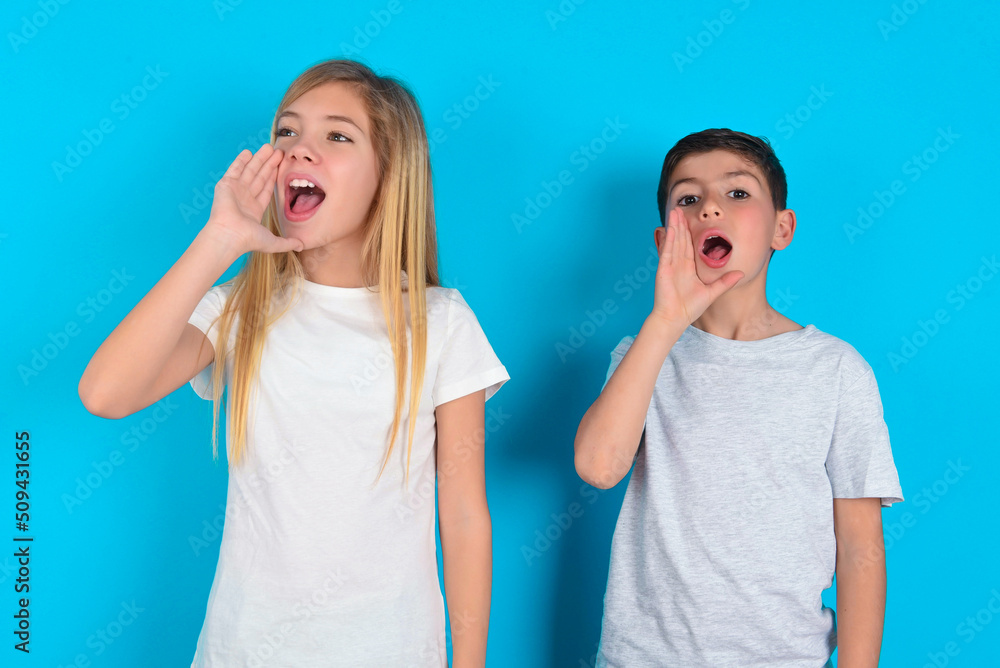 two kids boy and girl standing over blue studio background profile view, looking happy and excited, shouting and calling to copy space. two kids boy and girl standing over blue studio background profile view, looking happy and excited, shouting and calling to copy space.