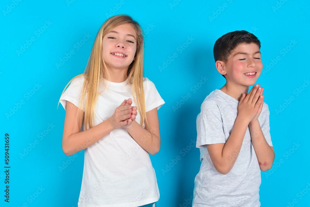 two kids boy and girl standing over blue studio background, feeling happy, smiling and clapping hands, saying congratulations with an applause. two kids boy and girl standing over blue studio background, feeling happy, smiling and clapping hands, saying congratulations with an applause.