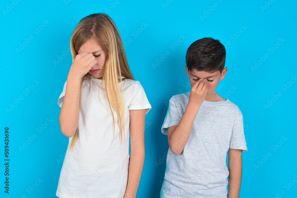 Very upset, two kids boy and girl standing over blue studio background touching nose between closed eyes, wants to cry, having stressful relationship or having troubles with work Very upset, two kids boy and girl standing over blue studio background touching nose between closed eyes, wants to cry, having stressful relationship or having troubles with work
