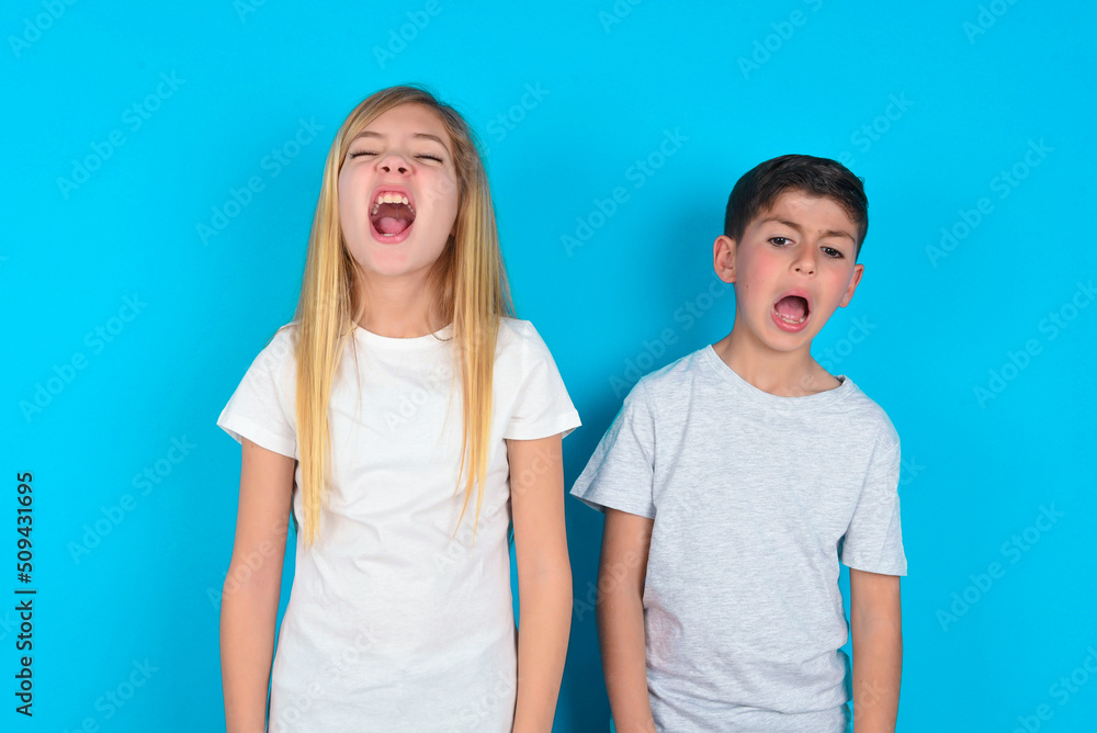 Stressful two kids boy and girl standing over blue studio background screams in panic, closes eyes in terror, keeps hands on head, finds out terrified news, can't believe it. Stressful two kids boy and girl standing over blue studio background screams in panic, closes eyes in terror, keeps hands on head, finds out terrified news, can't believe it.