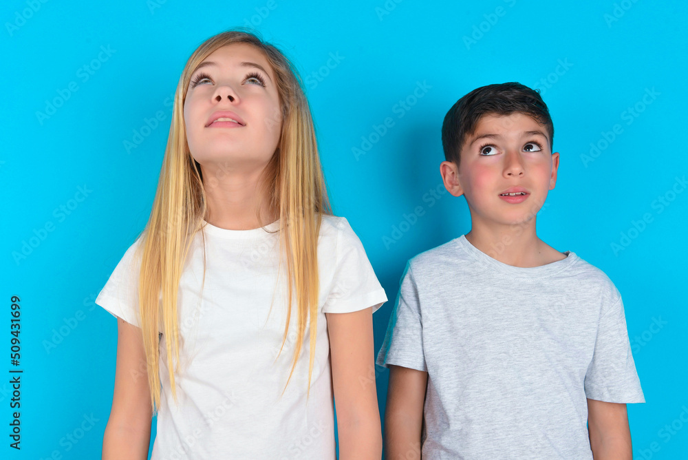 two kids boy and girl standing over blue studio background looking up as he sees something strange. two kids boy and girl standing over blue studio background looking up as he sees something strange.