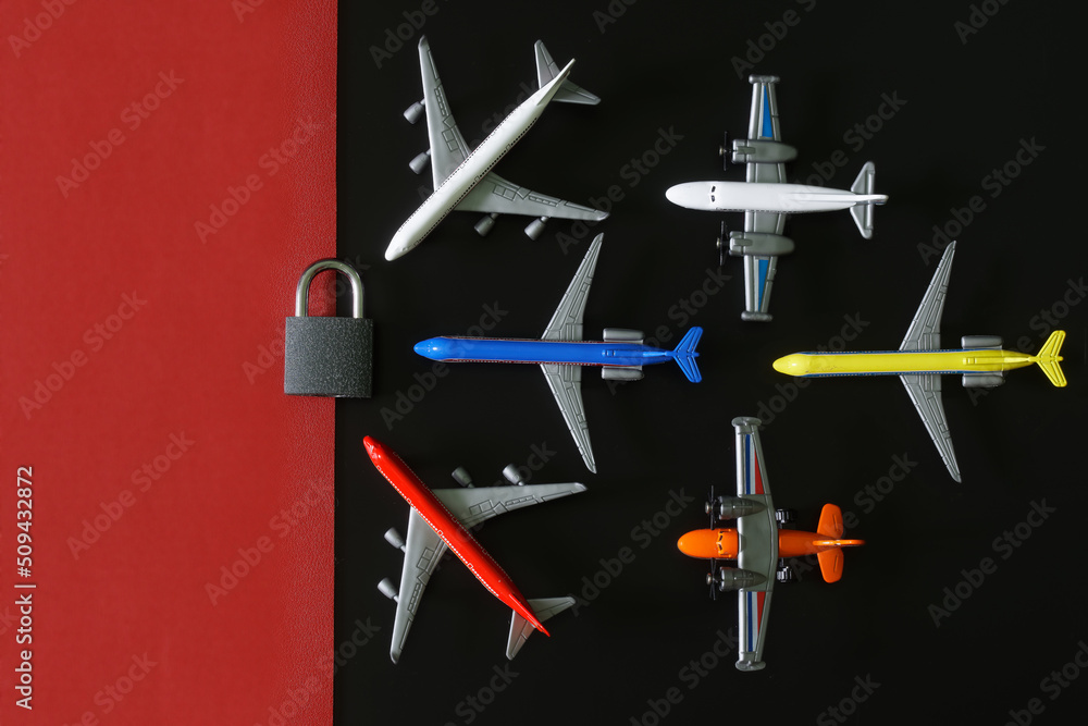 Six toy planes next to a padlock on a black and red background. Concept of sanctions and embargo on air flights and no-fly zone. Non-flying weather. Copy space. Six toy planes next to a padlock on a black and red background. Concept of sanctions and embargo on air flights and no-fly zone. Non-flying weather. Copy space.