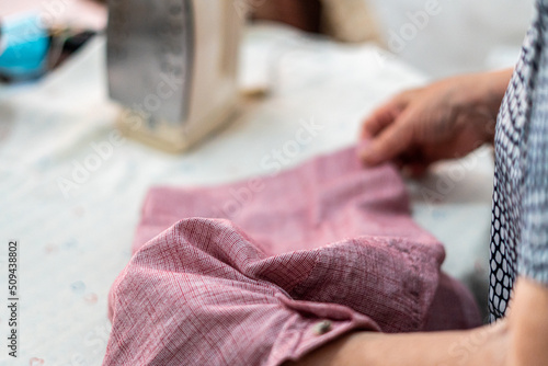 Lifestyle scene, unrecognizable woman with a t-shirt in her hands ready to iron.