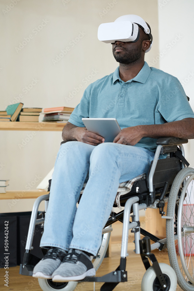 African AMerican man in VR goggles sitting in wheelchair using digital tablet for virtual reality therapy African AMerican man in VR goggles sitting in wheelchair using digital tablet for virtual reality therapy