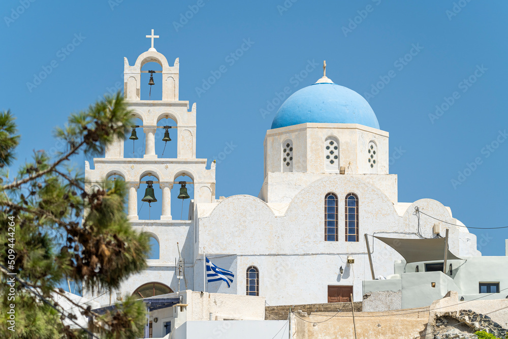 Blue and white colored Greek orthodox church, bells and cross roof, during a sunny summer day