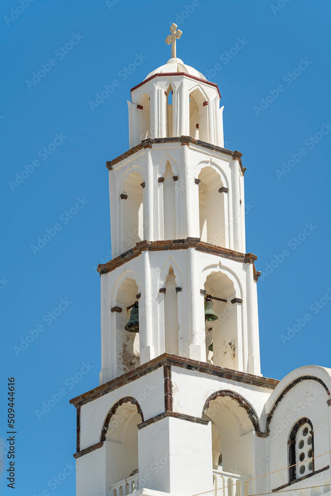 White colored greek orthodox church with bells and roof cross during a sunny summer day