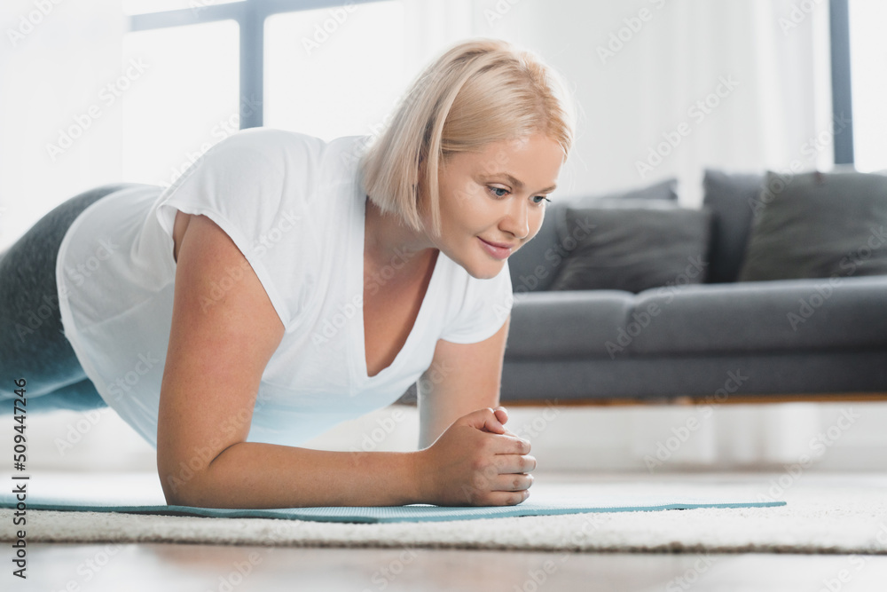 Closeup cropped young caucasian plus size plump woman athlete in fitness clothes standing in plank position, training stamina, slimming, burning calories at home Closeup cropped young caucasian plus size plump woman athlete in fitness clothes standing in plank position, training stamina, slimming, burning calories at home