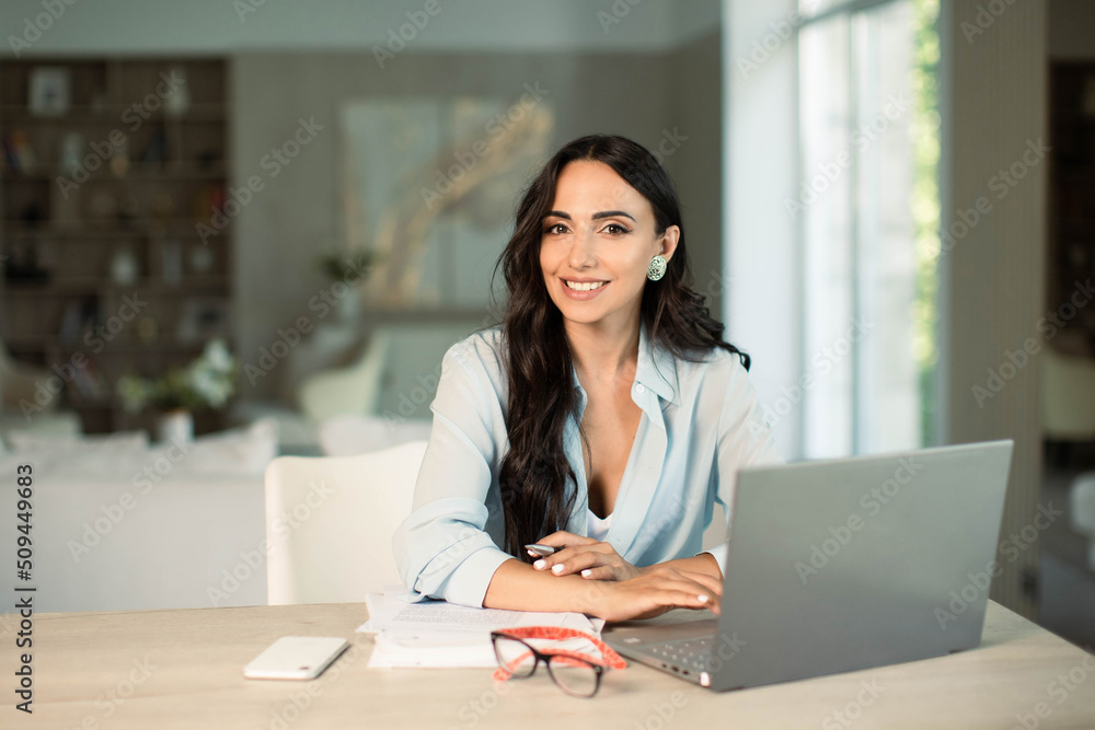 Smiling successful female using laptop computer indoors at home office, making notes on papers, remote work and small business freelancer, education and student. Smiling successful female using laptop computer indoors at home office, making notes on papers, remote work and small business freelancer, education and student.