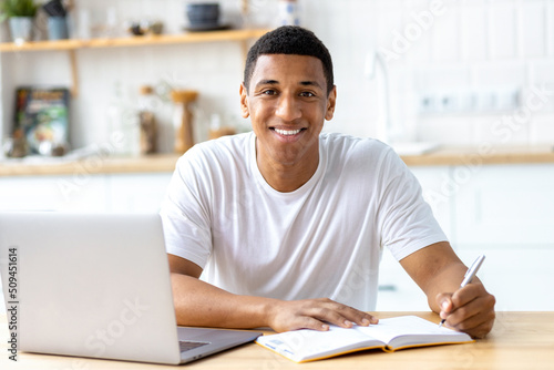 Smiling African american male student or freelancer studying remotely from home, using a laptop looks at the camera and smiles friendly. Online lesson, e-learning at home concept