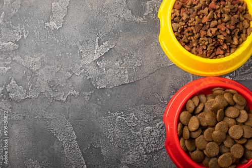 Dry food for cats and dogs in a yellow and red bowl on cement background.Vitamins and nutrients for good health and pet energy.