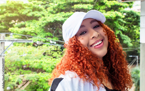 beautiful overweight teen girl smiling at camera in white cap and red curly hair outdoors happy © anderson