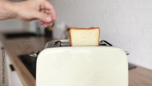 close up of hand are puting toasts bread in toaster in the kitchen. Includes kitchen appliance for making croutons and toasts for breakfast. A man's hand shoves a slice of bread into a toaster.