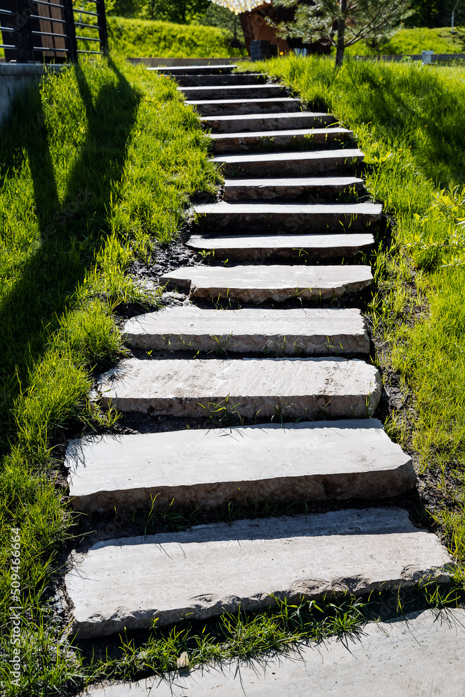 A staircase made of concrete steps in the park, urban landscape design, steps rise up, a path of their concrete, a sidewalk and a green lawn.