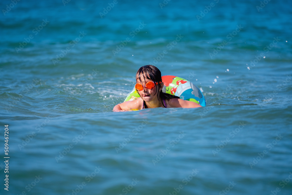 Portrait of beautiful young child girl on breaking wave. Kid in danger during sea swimming.