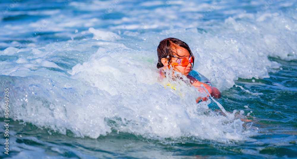 Portrait of young child girl on breaking wave. Kid in danger during sea swimming.