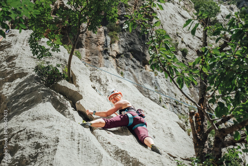 Smiling athletic woman in protective helmet climbing cliff rock wall using top rope and climbing harness in Paklenica National park site in Croatia. Active extreme sports time spending concept. photo