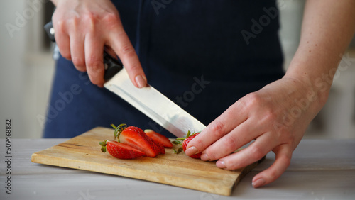 The hands of the cook cutting fresh strawberries in the kitchen for cooking