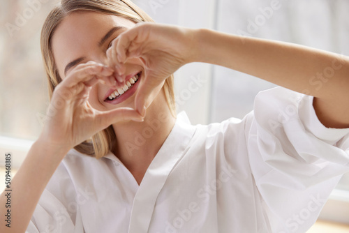 Healthy Tooth. Smiling Woman Showing Heart Sign wit Hands. Beautiful Happy Girl Model with Healthy White Smile and Natural Makeup. Stomatology and Teeth Care concept photo