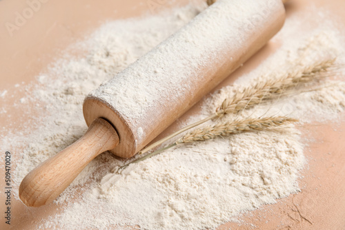 Rolling pin and wheat flour on color background, closeup