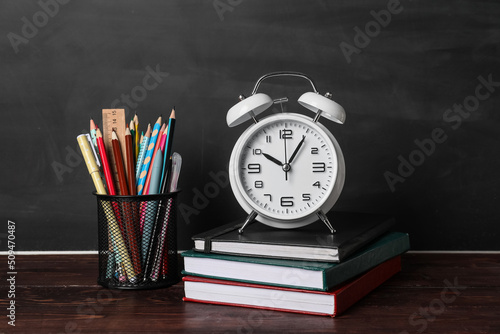 School stationery with alarm clock on table near blackboard