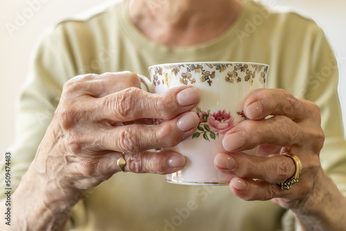 Image of an elderly woman with arthritis in her hands trying to hold a beautiful tea cup. Her fingers are twisted and contrast against the delicate tea cup. photo