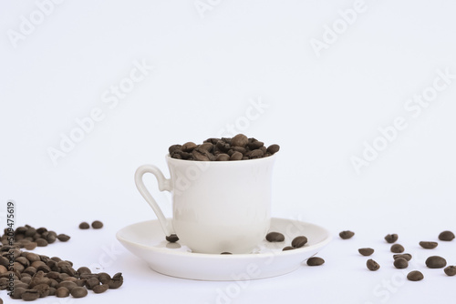 Coffee beans are spread around a white cup and saucer on a white background
