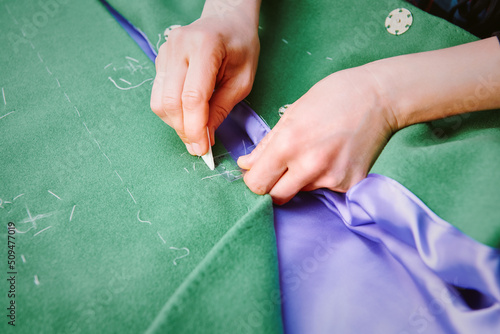 Tailor makes markings for buttons with chalk on the on green coat. Clothes sewing. Clothing repair. Tailoring. Close up view